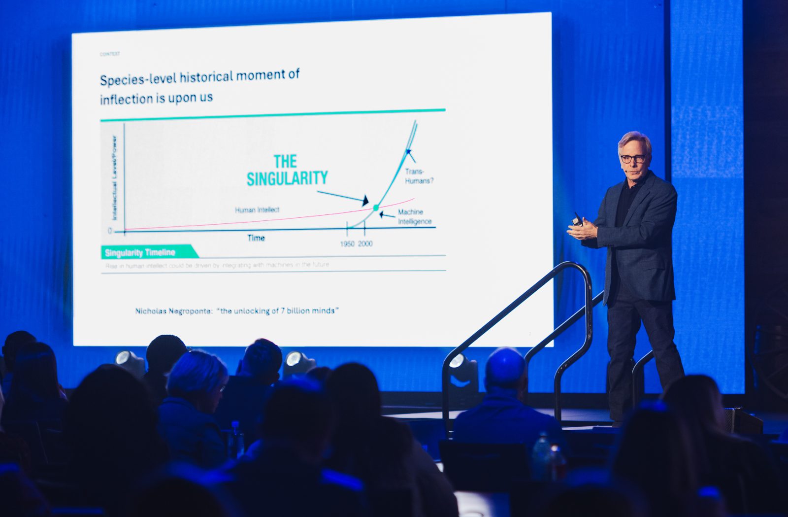 Fred Goff speaking on stage about the species-level moment of inflection, beside an exponential-curve slide